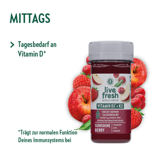 Eine Flasche „live fresh“ Vitamin D3 + K2 Shot mit der Geschmacksrichtung „Sunshine Berry“. Um die Flasche sind Erdbeeren, Cranberries und Äpfel arrangiert. Der Text betont die Versorgung mit Vitamin D für das Immunsystem und den Erhalt normaler Knochen.