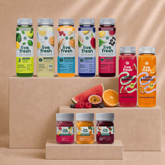 Live Fresh Balance Kur mit verschiedenen Säften und Shots auf beigen Podesten. Zu sehen sind unter anderem Grüne Gefühle, Happy Lemon, Hey Wach, Keep Cool, Kombucha Ritual sowie Daily Balance Drinks und Immun Shots mit frischem Obst.