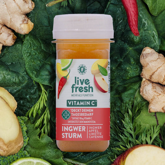 LiveFresh Shot „Ingwer Sturm“ mit Vitamin C zur täglichen Immununterstützung. Der Shot liegt zwischen Ingwer, Apfel, Limette und Cayenne-Pfeffer auf einem grünen Blattbett.