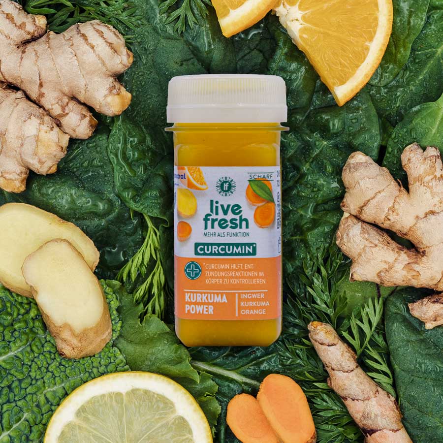 Flasche LiveFresh namens Kurkuma Power auf grünem Gemüsebett mit Ingwer, Kurkuma, Orange und Zitrone – beworben zur Unterstützung von Entzündungsreaktionen.