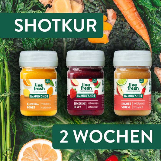 Drei LiveFresh Immun Shots Kurkuma Power Sunshine Berry und Ingwer Sturm auf dunklem Blattgemüse mit Gemüse und Orange. Darüber und darunter steht "Shotkur 2 Wochen".