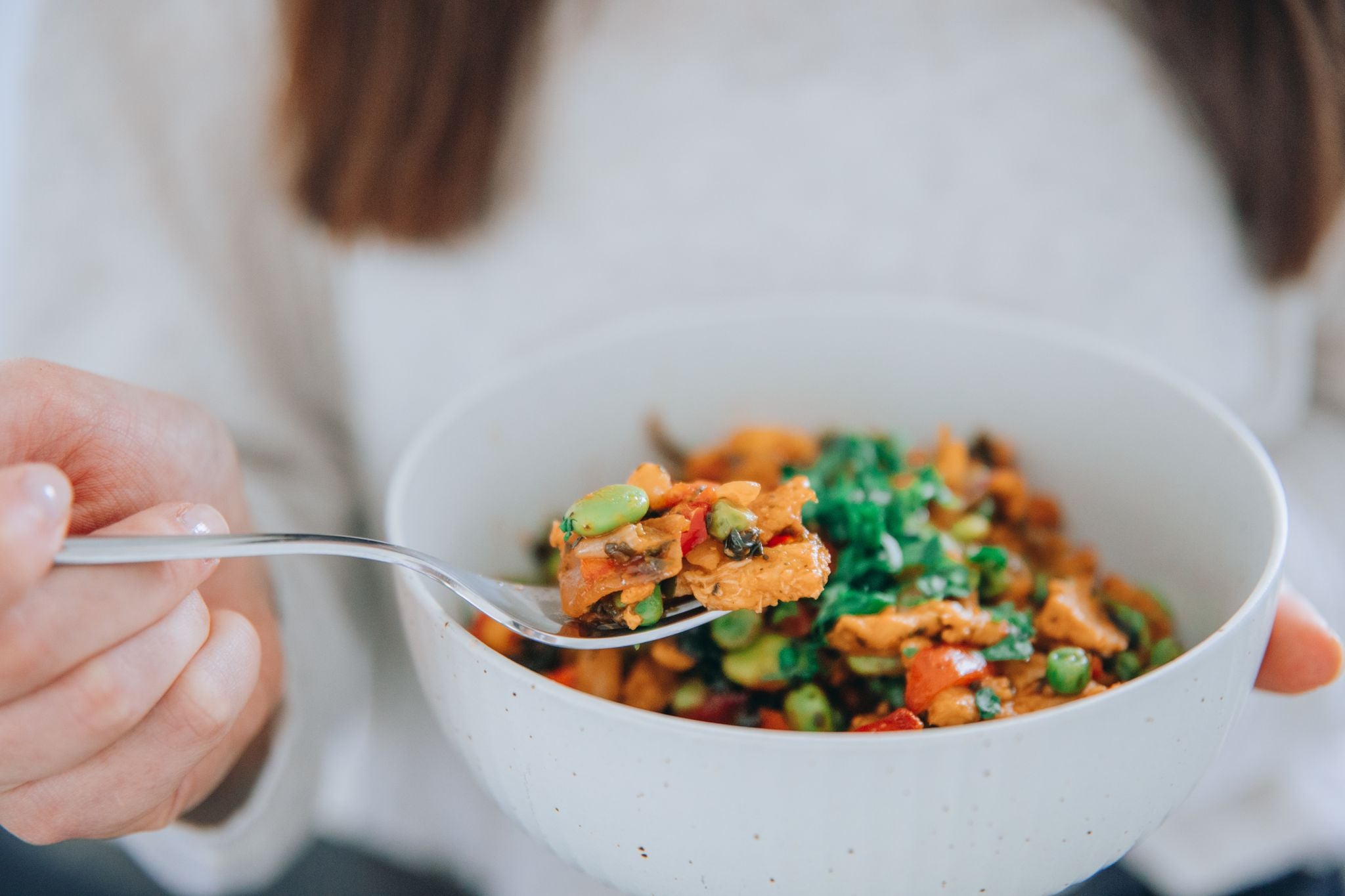 Eine Person hält eine Schüssel mit einem gesunden Rezept, das bunte Gemüse und Proteine enthält.