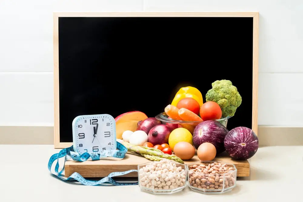 Lebensmittel, Eier und Gemüse neben Wecker und Maßband vor einer Tafel, symbolisieren Autophagie, intermittierendes Fasten und bewusste Ernährung.
