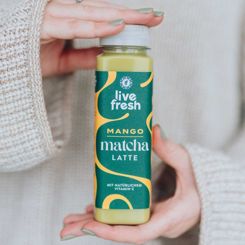 „Live Fresh“ Mango Matcha Latte Flasche zwischen zwei Händen.