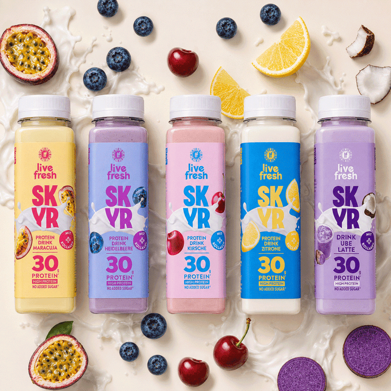 Fünf bunte Flaschen Skyr Proteindrink von Live Fresh in den Sorten Maracuja. Heidelbeere. Kirsche. Zitrone und Ube Latte. Rund um die Skyr Drinks liegen passende Früchte wie Maracuja. Heidelbeeren. Kirschen. Zitronen und Kokosnuss in Milchspritzern.