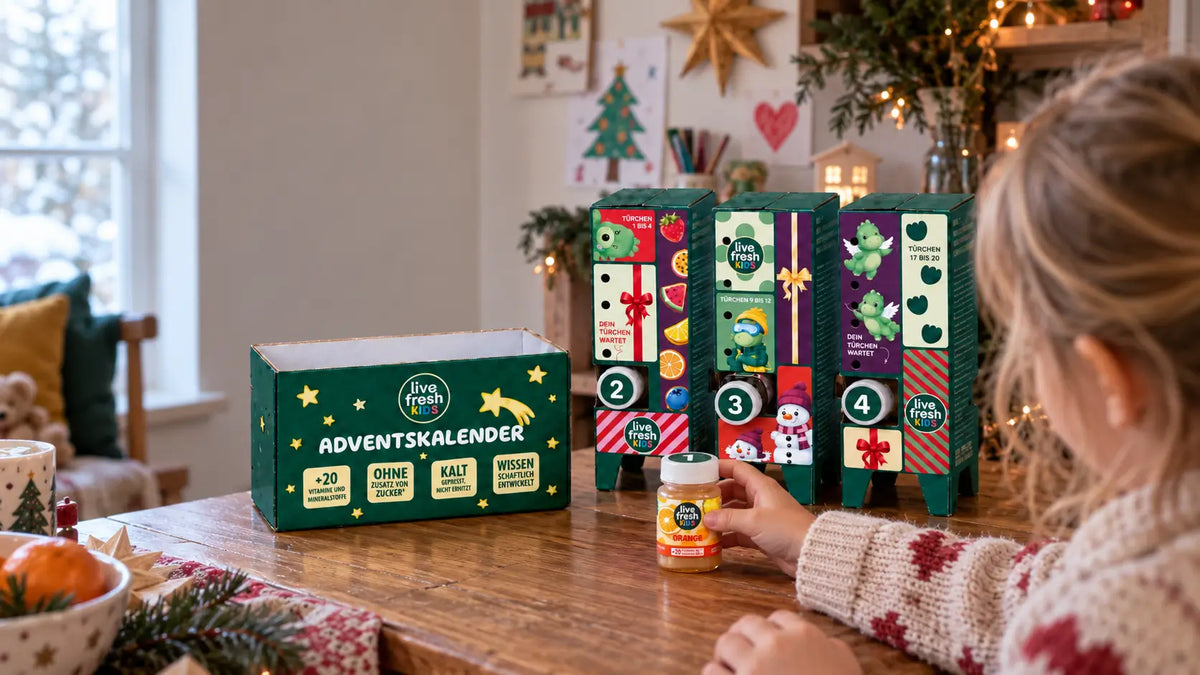 Ein Mädchen sitzt vor dem geöffneten LiveFresh Kids Adventskalender und hält die orangefarbene Flasche aus Türchen eins. Auf dem Kalender steht "ADVENTSKALENDER" sowie "+20 VITAMINE UND MINERALSTOFFE" "OHNE ZUSATZ VON ZUCKER" "KALT GEPRESST NICHT ERHITZT" und "WISSENSCHAFTLICH ENTWICKELT".
