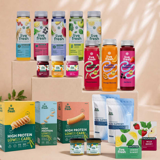 Große Auswahl an LiveFresh Produkten auf beigefarbenen Podesten. Zu sehen sind Säfte Daily Balance Drinks Immun Shots High Protein Lower Carb Produkte Slim Support Gemüsebrühe sowie Grüntee Lemon Mint und Früchtetee Wild Berry.