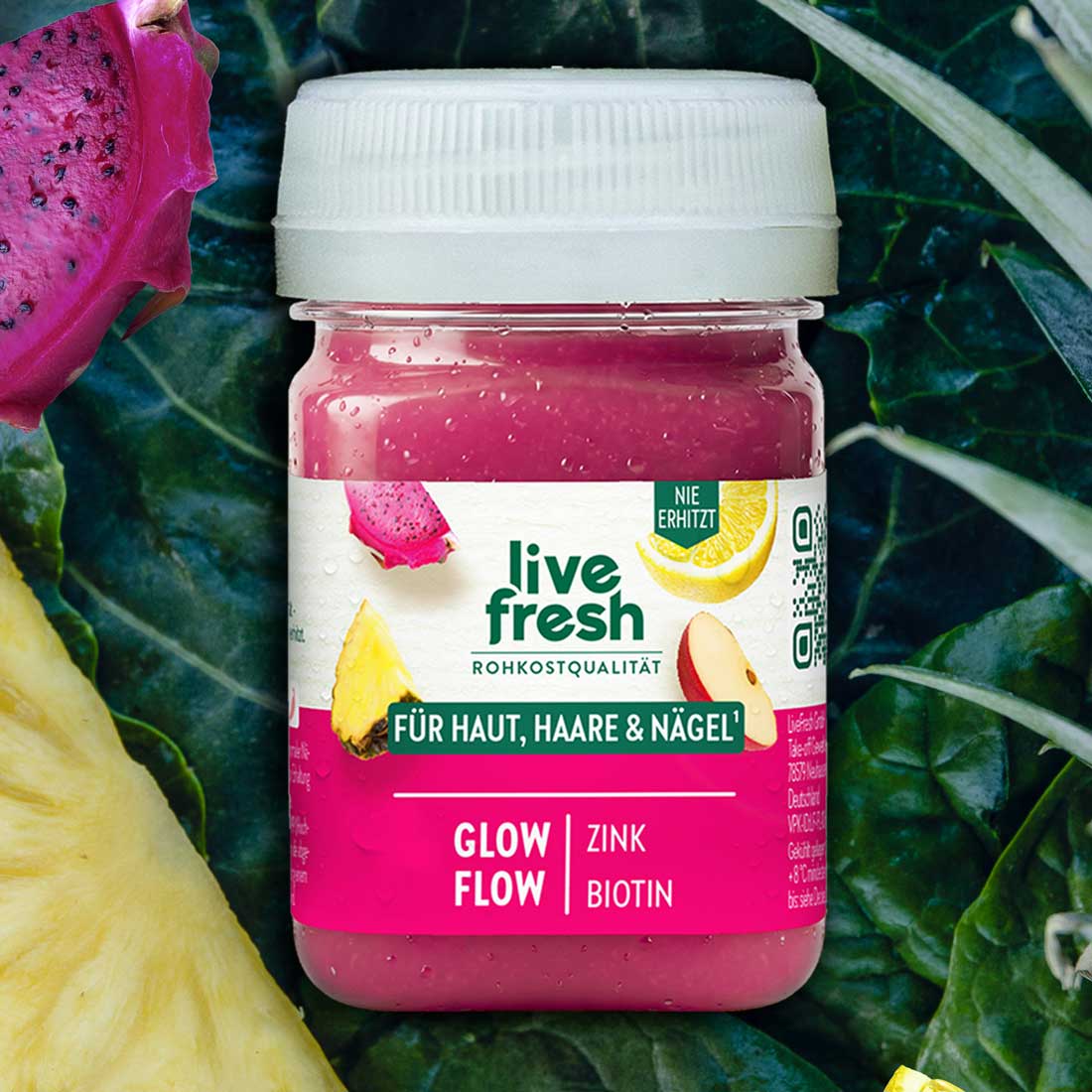 Pinker LiveFresh Shot zwischen dunklem Blattgemüse Drachenfrucht und Ananas. Auf dem Etikett steht "live fresh Rohkostqualität Für Haut Haare und Nägel Glow Flow Zink Biotin".