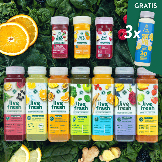 Verschiedene bunte Live Fresh Saftflaschen und Shots liegen auf grünem Blattgemüse neben Orangen, Zitronen, Ingwer und Beeren. Auf den Flaschen stehen Sorten wie „Kombucha Ritual“, „Happy Lemon“, „Gold Rausch“, „Grüne Gefühle“, „Hey Wach“, „Keep Cool“ und „Sommer Gefühle“, rechts daneben der Hinweis „Gratis 3x Skyr Protein Drink Zitrone 30g Protein“.