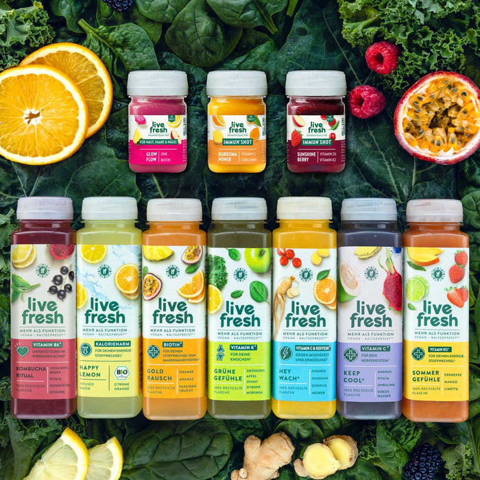 Auswahl aus drei LiveFresh Shots und sieben bunten Säften auf dunklem Blattgemüse mit Orangen Himbeeren Maracuja Limetten Ingwer und Brombeeren. Die Produkte zeigen verschiedene Sorten von Glow Flow und Sunshine Berry bis Kombucha Ritual Happy Lemon Gold Rausch Grüne Gefühle Hey Wach Keep Cool und Sommer Gefühle.