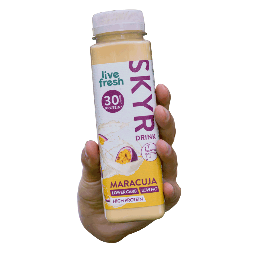 Eine Hand, die einen Live Fresh Skyr Drink in der Geschmacksrichtung Maracuja hält. Der Drink enthält 30g Protein, ist fettarm und kohlenhydratarm.