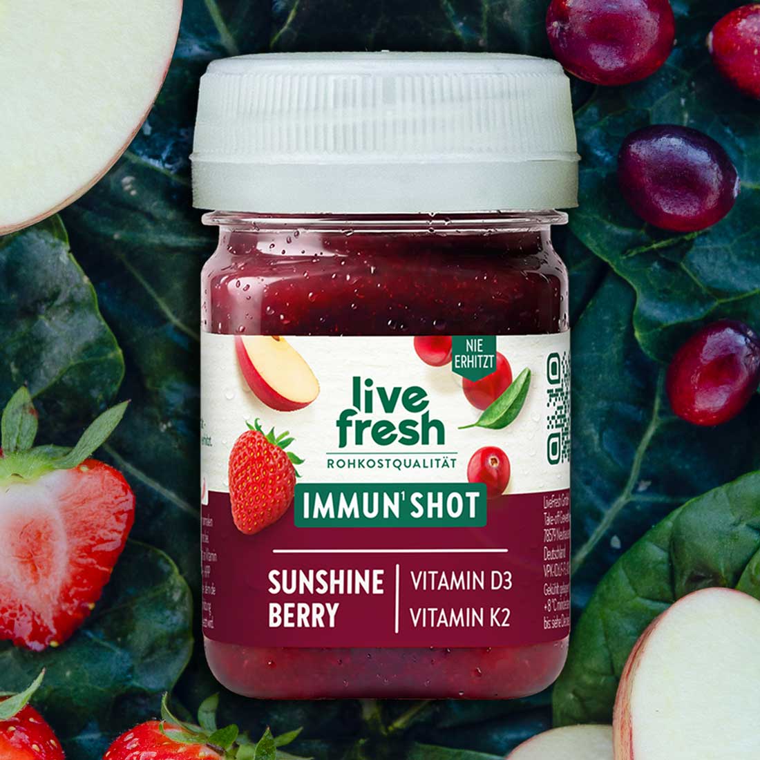 Dunkelroter LiveFresh Immun Shot zwischen Blattgemüse Erdbeeren Äpfeln und roten Beeren. Auf dem Etikett steht "live fresh Rohkostqualität Immun Shot Sunshine Berry Vitamin D3 Vitamin K2".