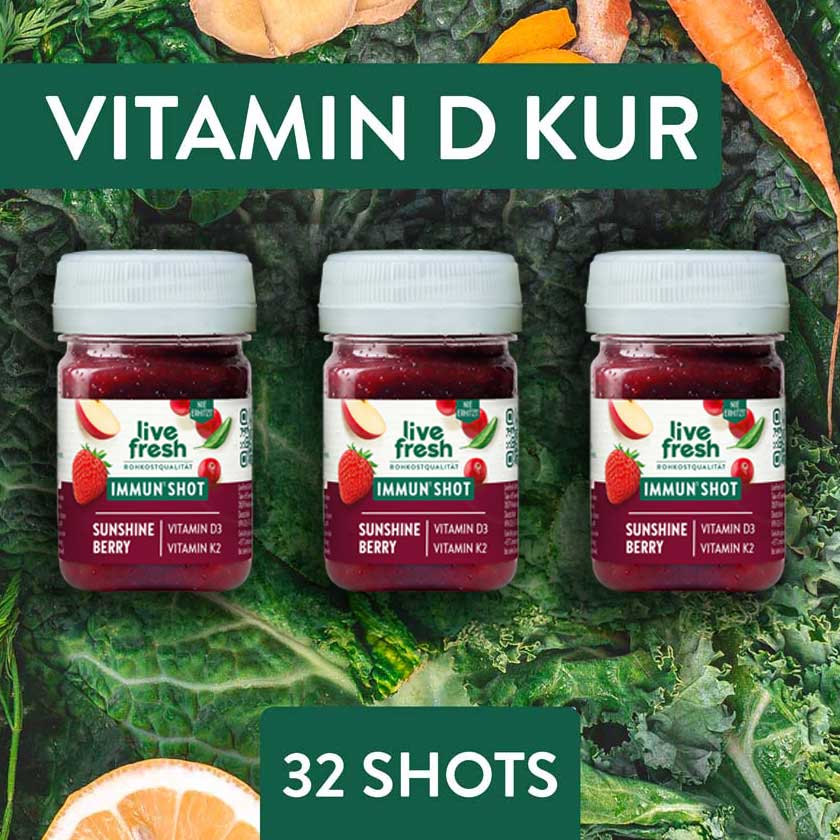 Drei LiveFresh Sunshine Berry Immun Shots auf dunklem Blattgemüse mit Ingwer Karotte und Orange. Im Motiv steht "Vitamin D Kur 32 Shots".
